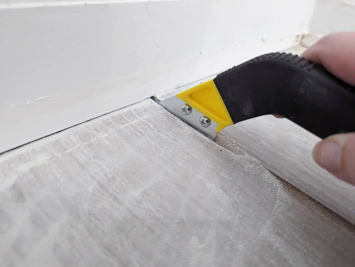 using a handheld grout saw to remove grout from tile floor.