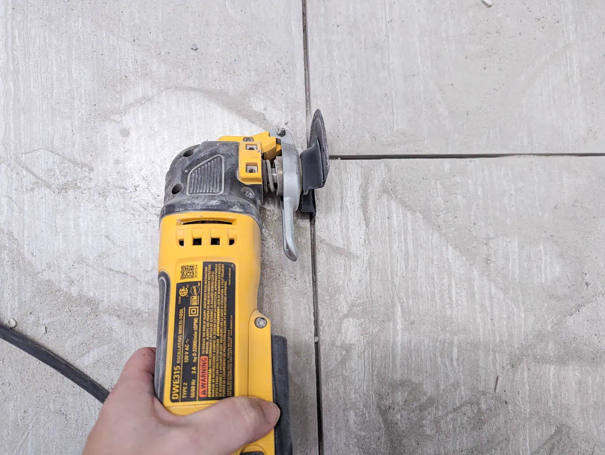 using an oscillating tool to remove grout from tile floor.