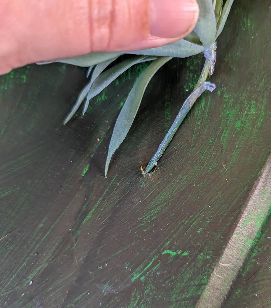 sliding the stem of a faux succulent into  a hole in cardboard.