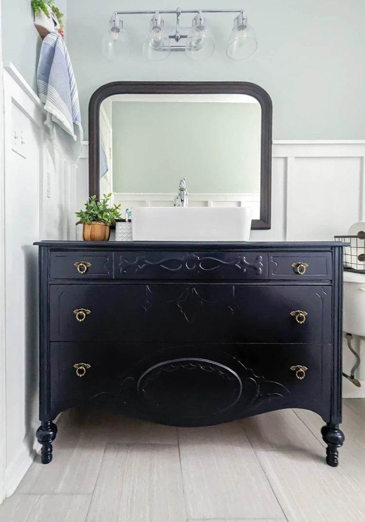 vintage dresser bathroom vanity with brass hardware and an arched wood mirror.