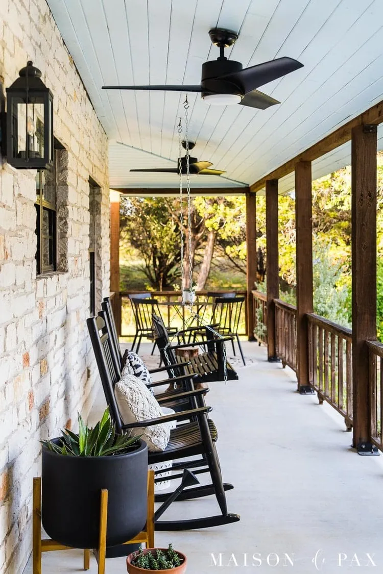 front porch with black rocking chairs next to a black porch swing.