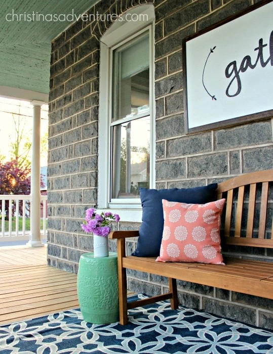front porch with bench and pillows beneath large wooden gather sign.