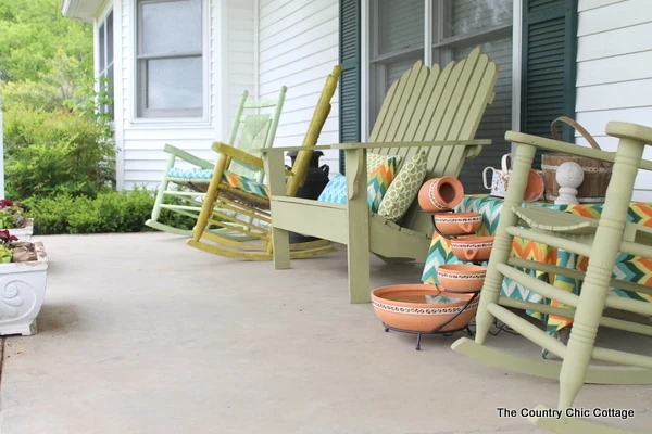 rocking chairs and adirondack chair on front porch all painted the same shade of green.