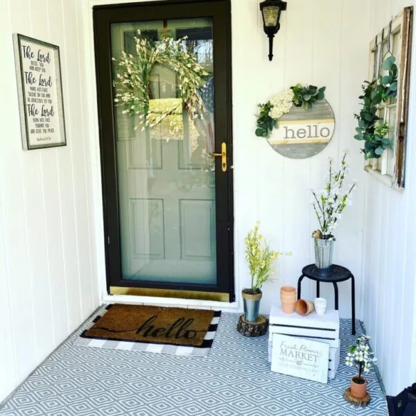 small front porch with several pieces of art on the wall and layered rugs in front of the door.
