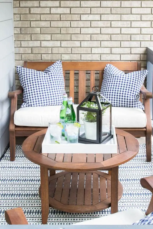 Small porch with wood furniture and tray with a lantern and drinks on table.