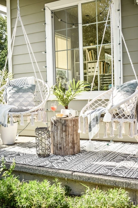 porch with two boho hanging chairs next to a stump table.