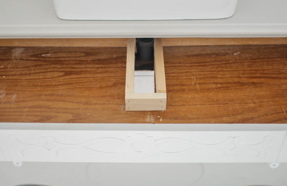 small hole cut into top drawer of dresser bathroom vanity with wood sides built around it.