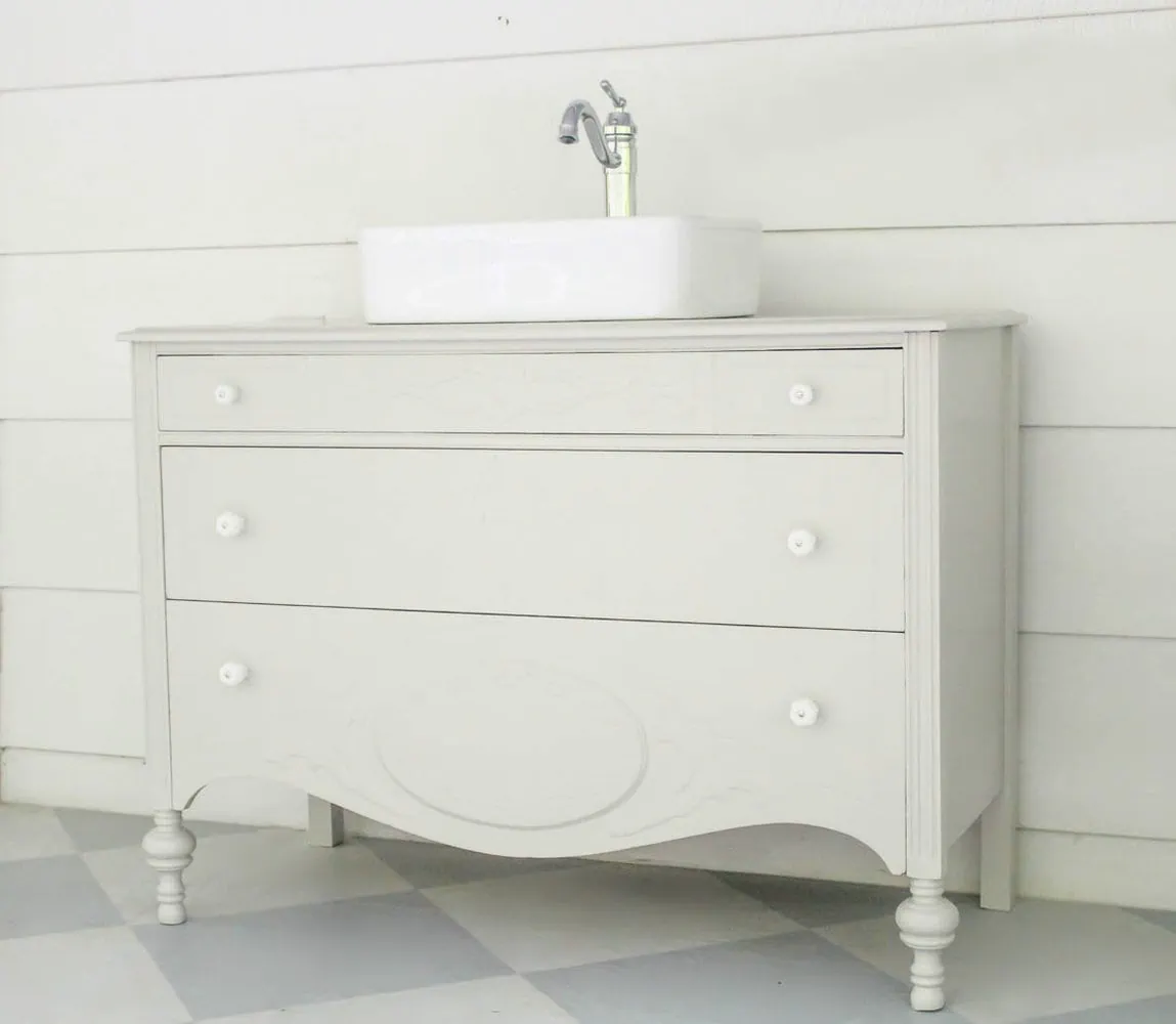 antique dresser turned into a bathroom vanity with a vessel sink on top, painted gray with white milk glass knobs.