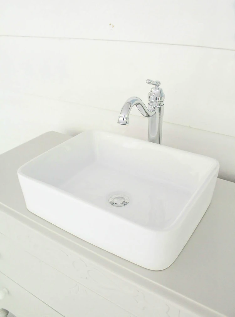 white rectangle vessel sink and chrome faucet on dresser bathroom vanity next to white shiplap wall.