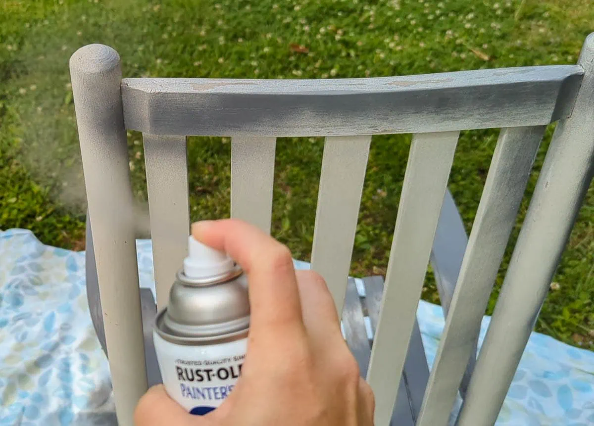 moving the spray paint can side to side while painting the back of a chair.