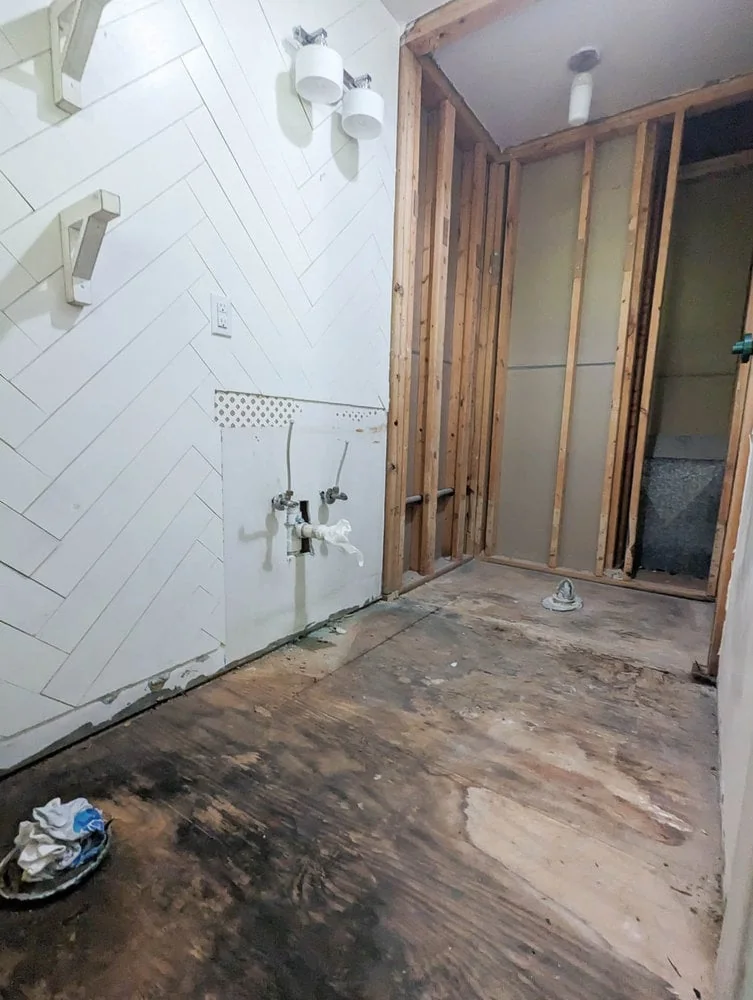 bathroom after demo with bare subfloors and stud walls.