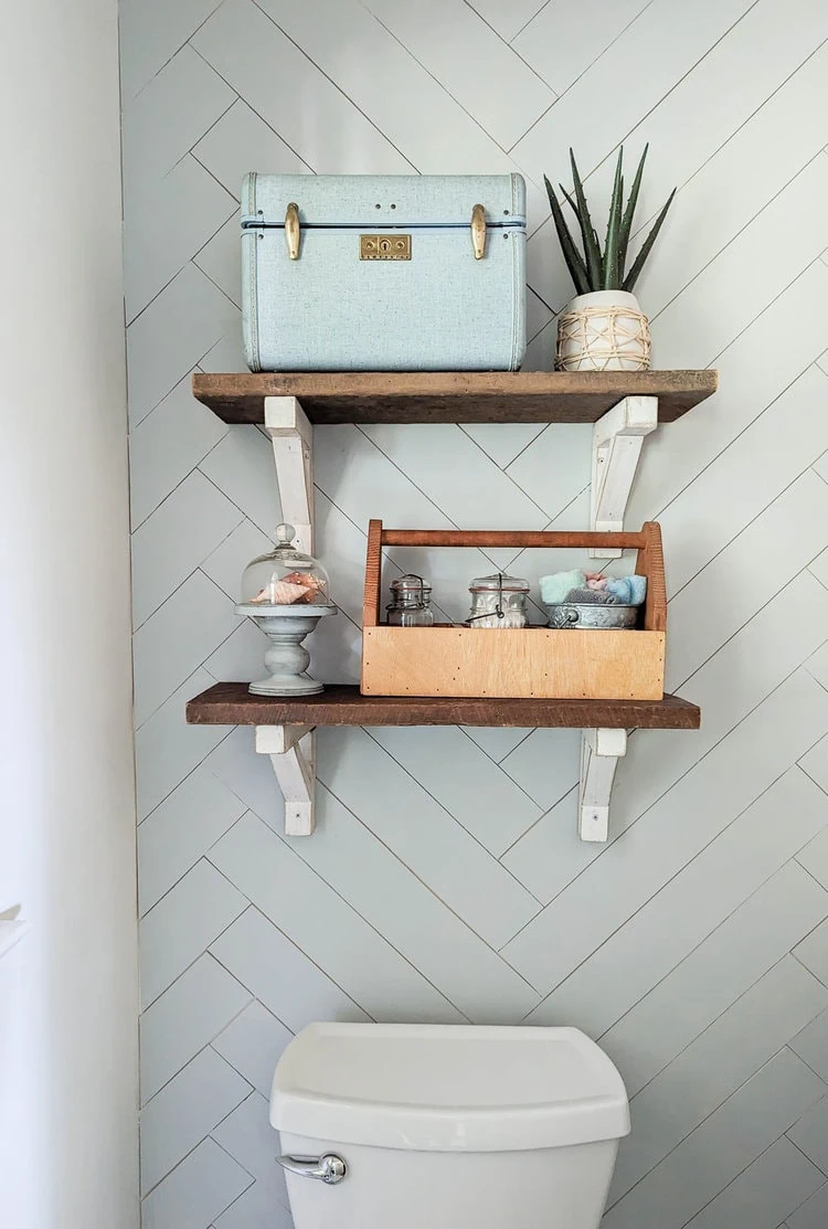 DIY wood shelves over toilet against wood wall painted a light greenish-gray.