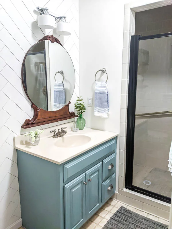 Master bathroom with painted vanity, wood accent wall, vintage mirror, and shower door painted black.