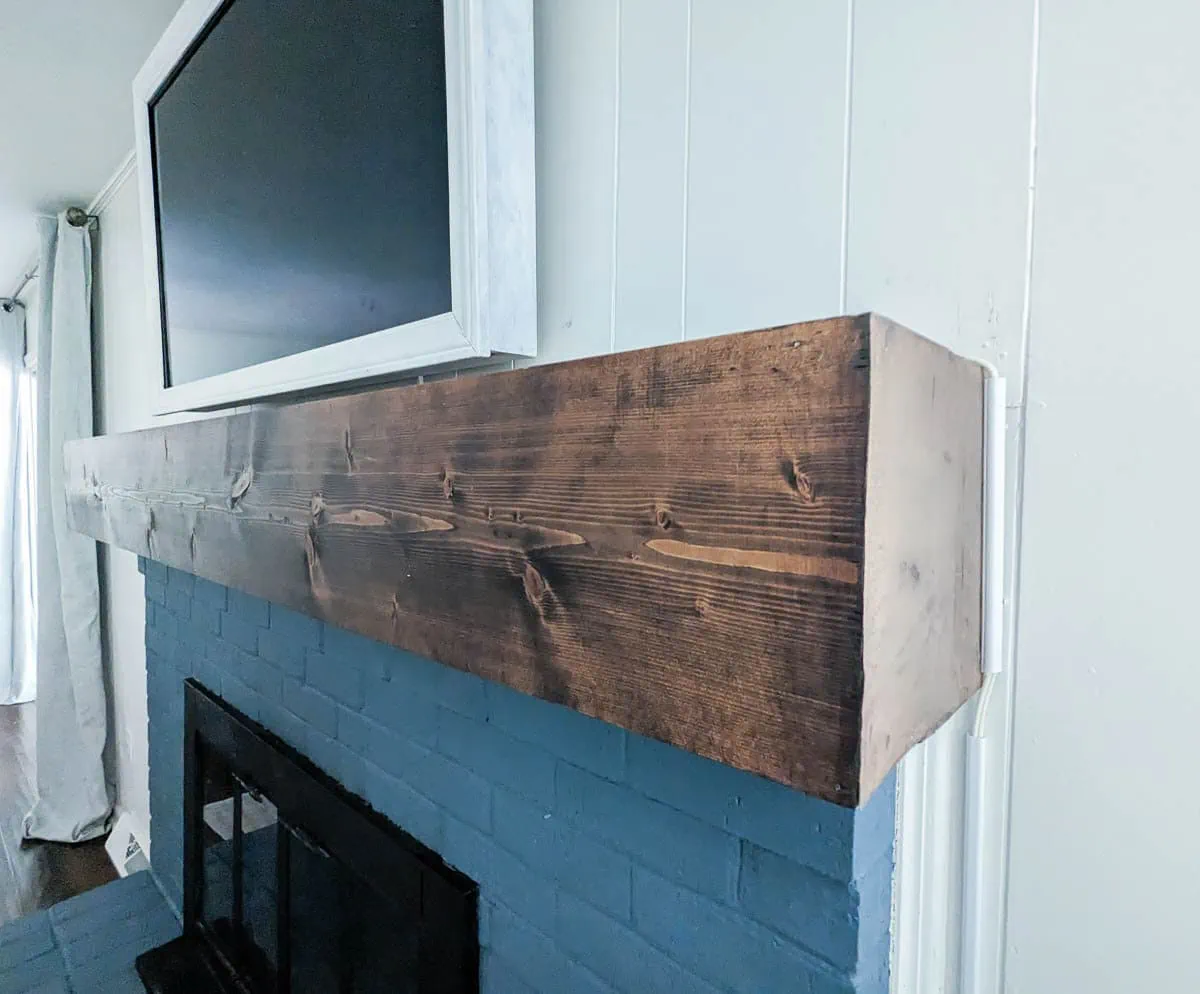 chunky wood mantel on blue brick fireplace.