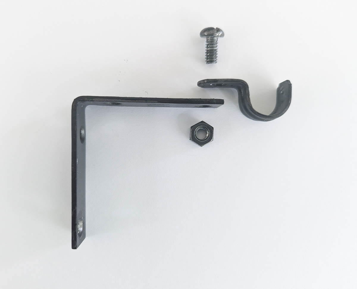 How to make cheap DIY Curtain rods using simple supplies from the hardware store. corner brace, pipe strap, nut, and bolt ready to make DIY curtain rod bracket.