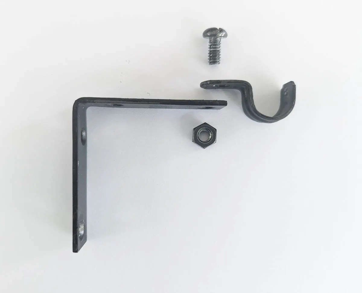 corner brace, pipe strap, nut, and bolt ready to make DIY curtain rod bracket.