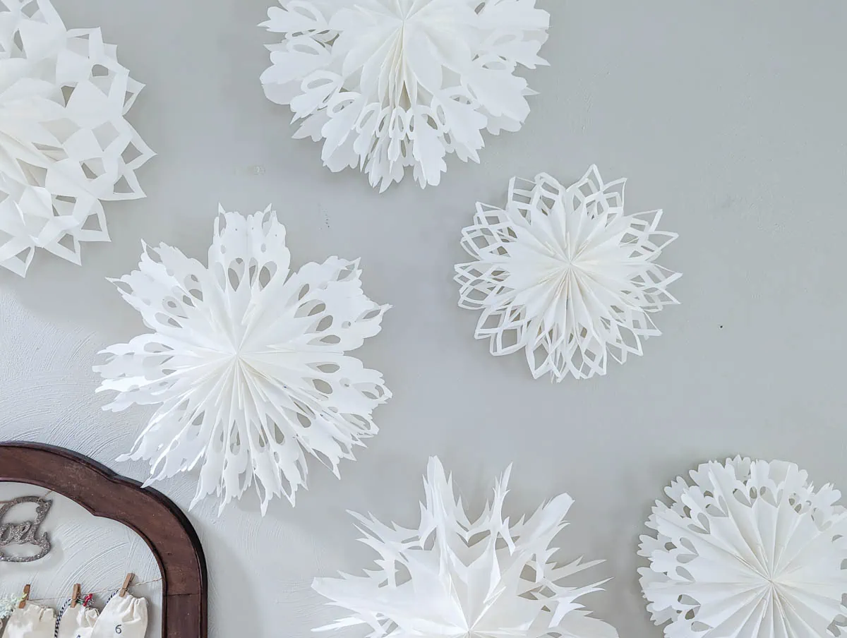 different paper bag snowflake designs hanging on wall with command hooks.