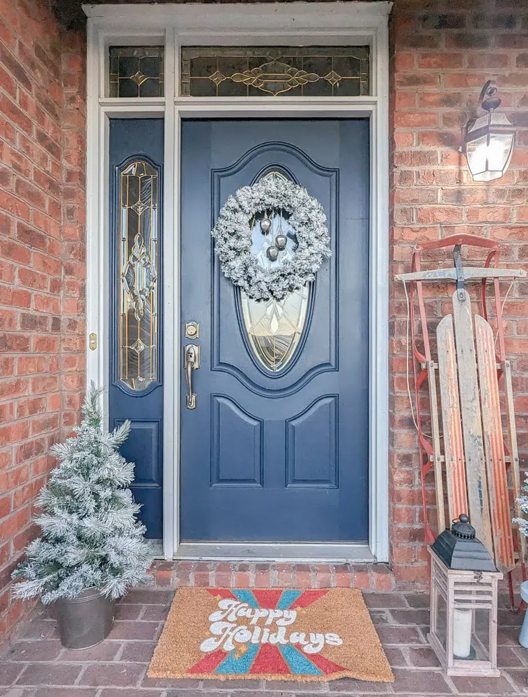 brick front porch decorated for Christmas with flocked wreath hanging on glass door.