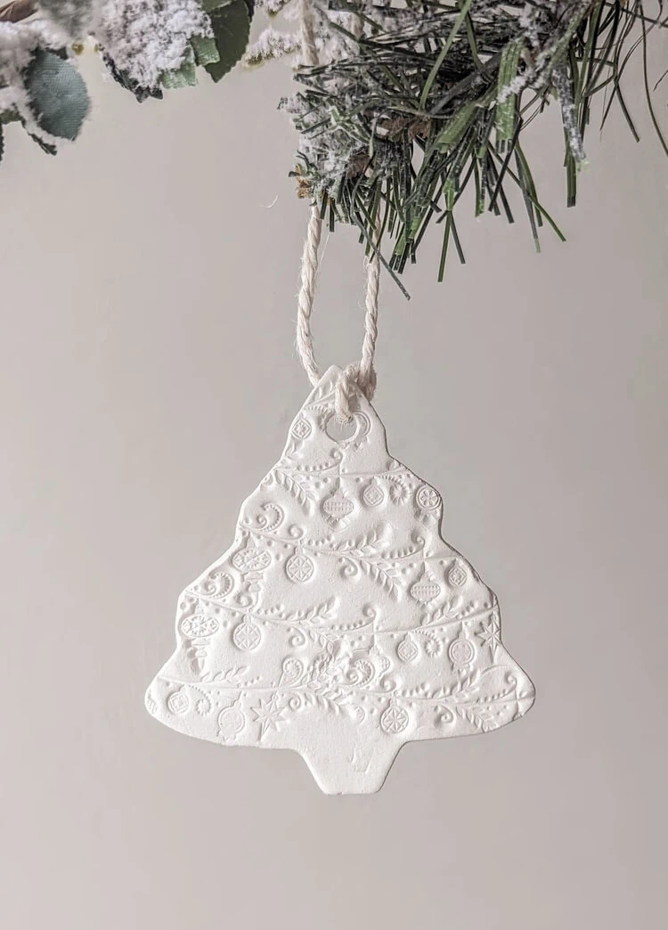 a clay ornament shaped like a Christmas tree with ornaments and garland stamped on.