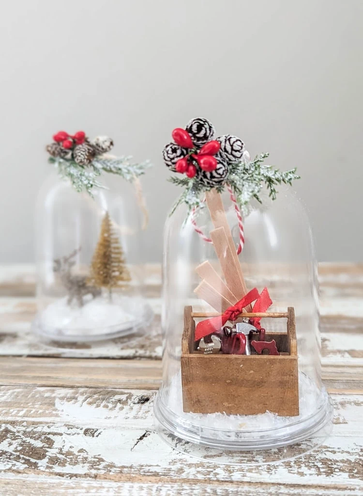 two diy snow globe ornaments - one with a mini toolbox and one with a deer and christmas tree.
