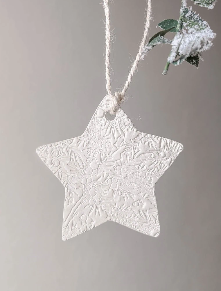 a clay Christmas ornament shaped like a star with a stamped holly texture.