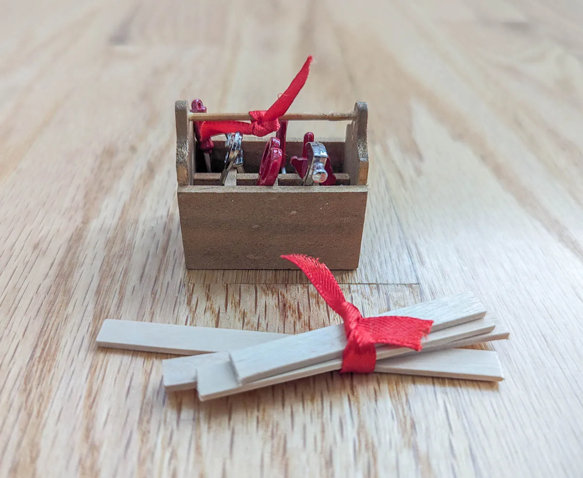 miniature toolbox with tiny tools and a small stack of wood ties with red ribbons.