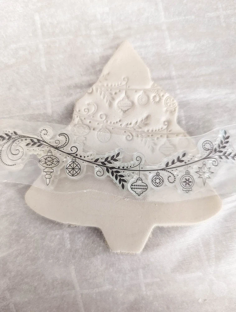 stamping ornament shapes onto a Christmas tree shaped clay ornament.