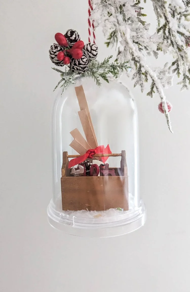 diy snow globe ornament with tiny toolbox and wood boards inside.