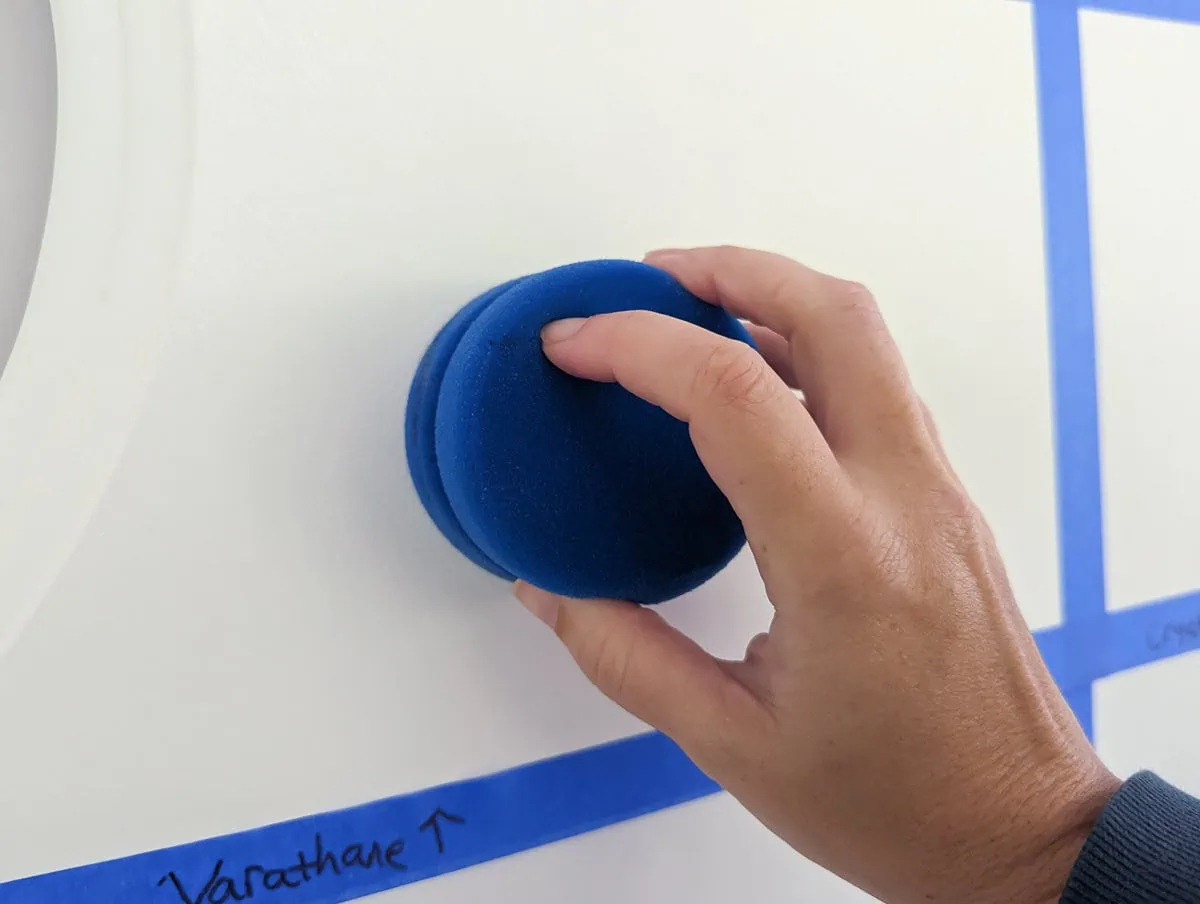 Applying sealer to a headboard using a blue sponge applicator.