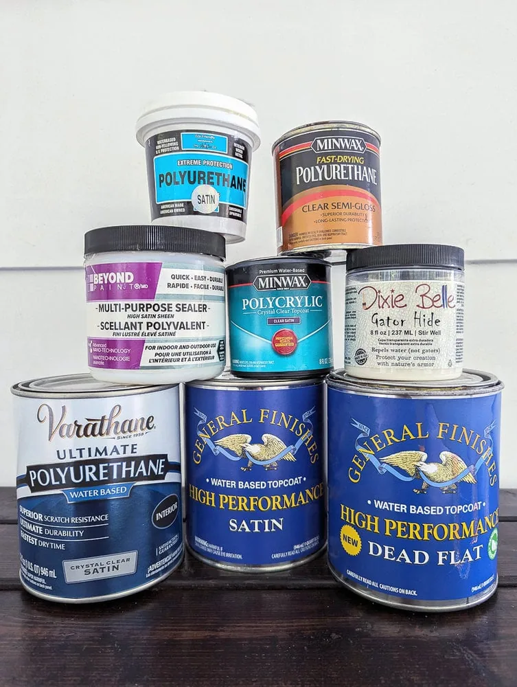 stack of furniture sealers including crystalac polyurethane, minwax polyurethane, beyond paint multi purpose sealer, minwax polycrylic, dixie belle gator hide, varathane polyurethane, and general finishes topcoat in satin and dead flat.
