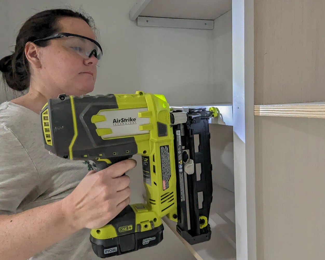 using a nail gun to attach the trim to closet shelves.