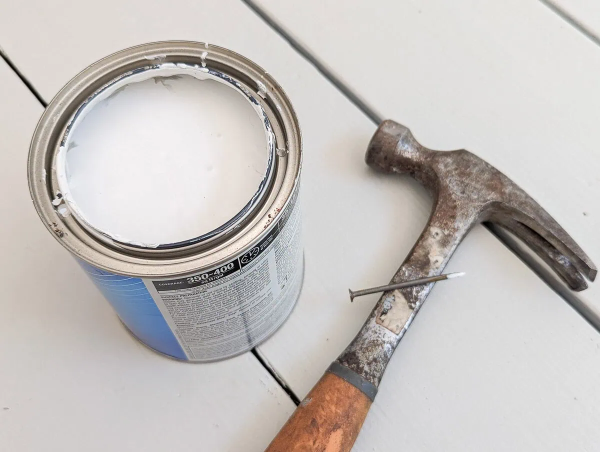 can of paint with holes in rim next to a hammer and a nail