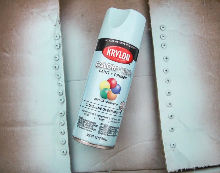 cardboard box with screws poked into box flaps next to a can of spray paint.