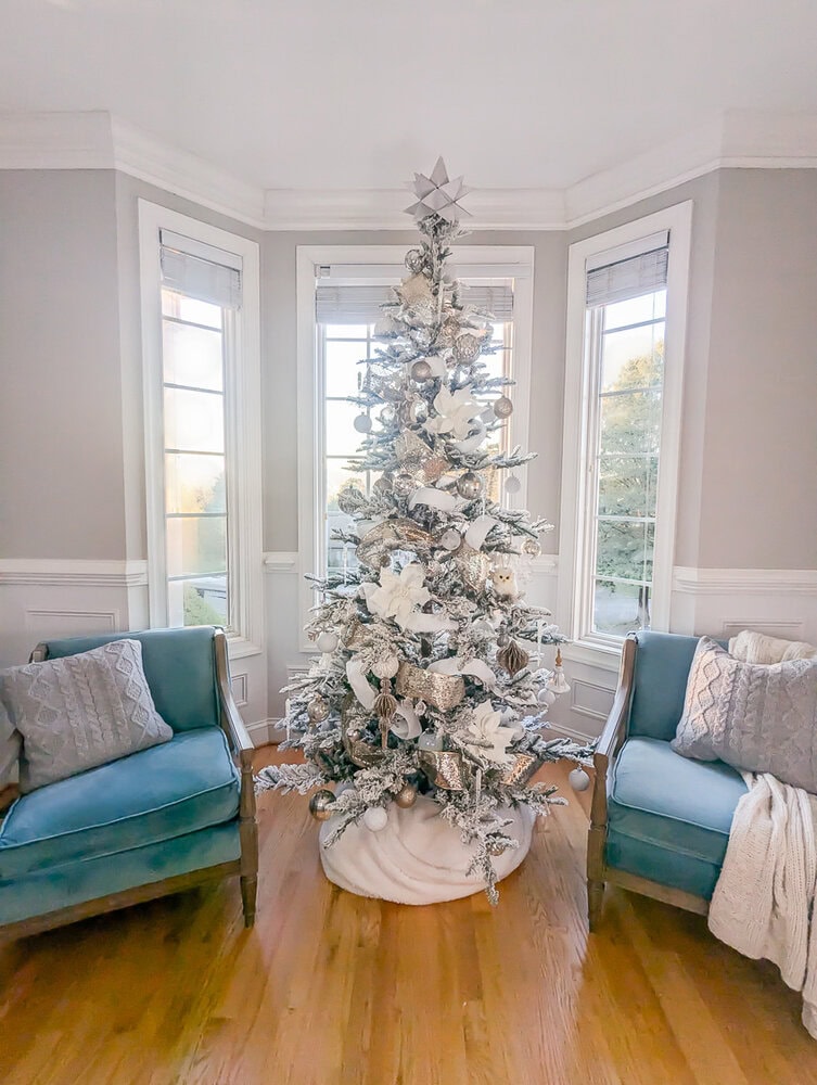 Silver and gold decorated Christmas tree between two blue chairs.