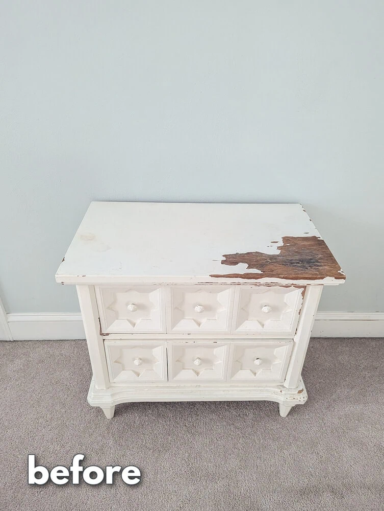 white nightstand with chipping paint and water damage.