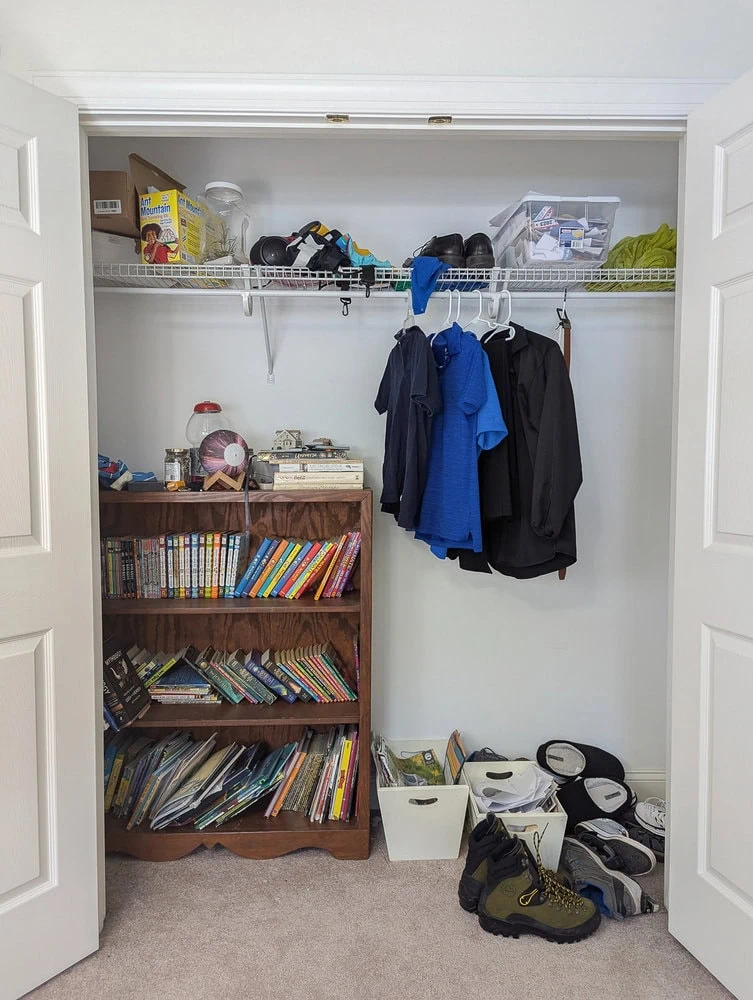 closet with a few shirts hanging and a bookcase inside.