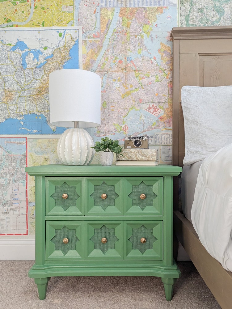 green painted nightstand next to bed in front of map wallpaper.