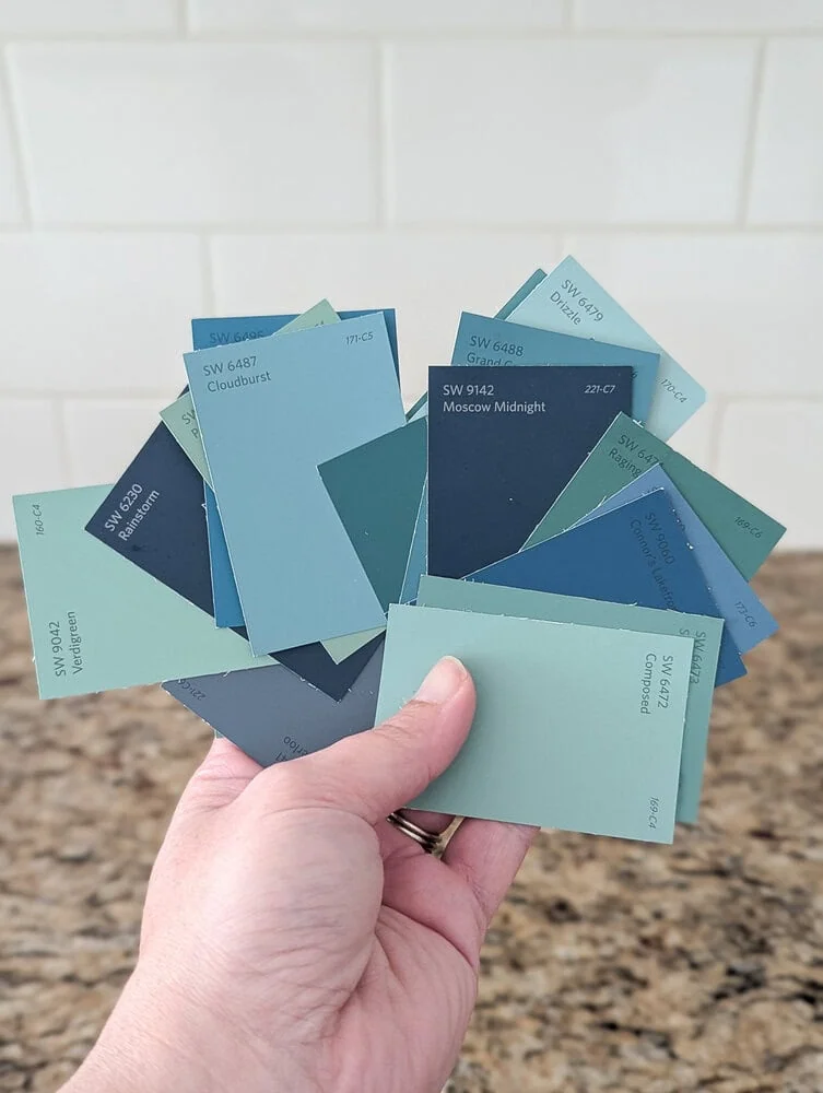 hand holding a variety of blue and green paint chips.