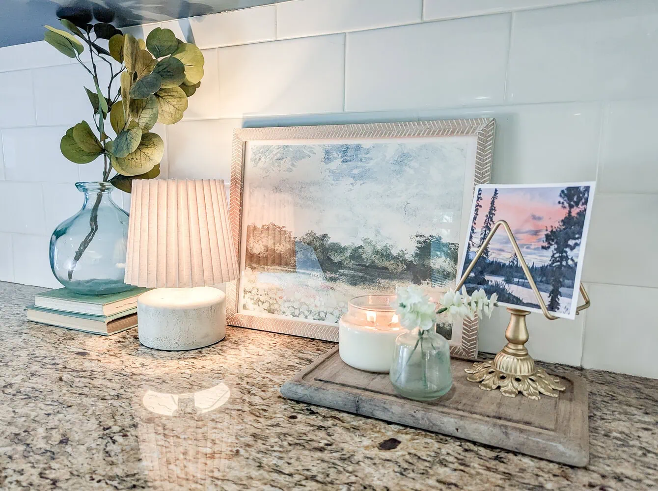 kitchen counter styled with lamp, candle, plants, and framed print.