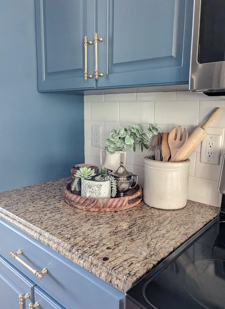 Kitchen counter with vintage crock filled with utensils and round wooden tray.