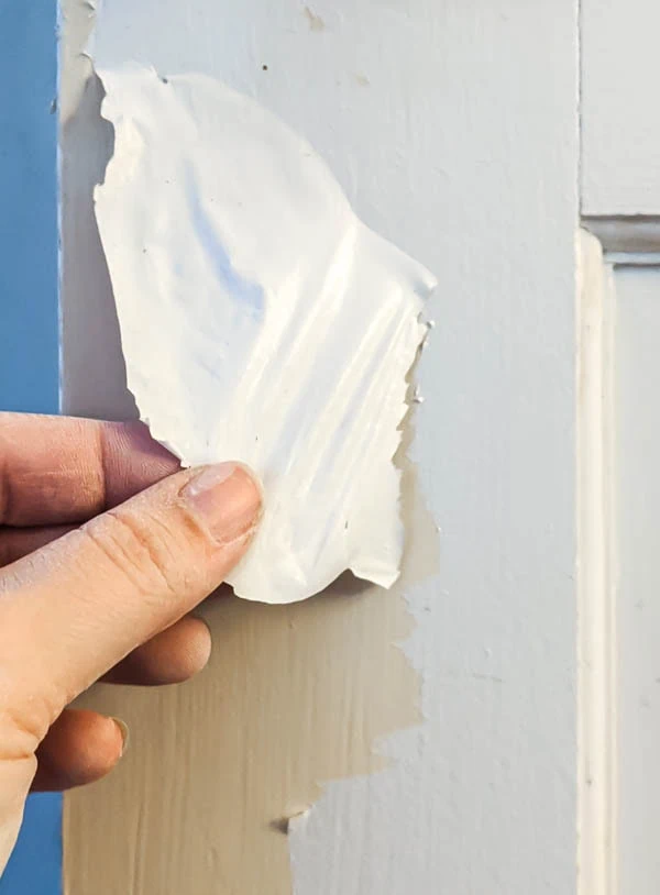 hand peeling a big piece of white latex paint off a door.