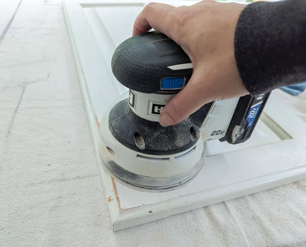 sanding a cabinet door with an orbital sander.