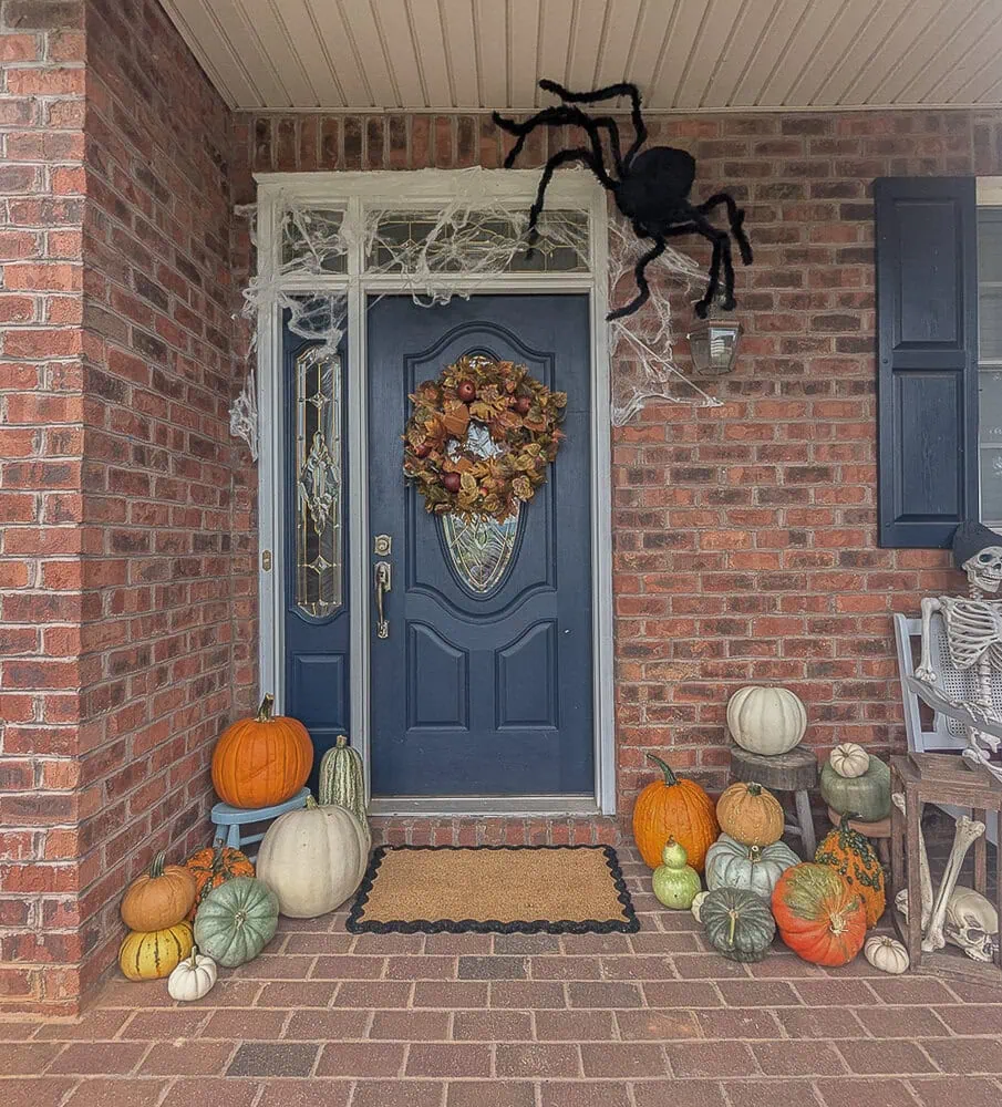 Halloween front porch with piles of pumpkins, huge spider, and skeleton.