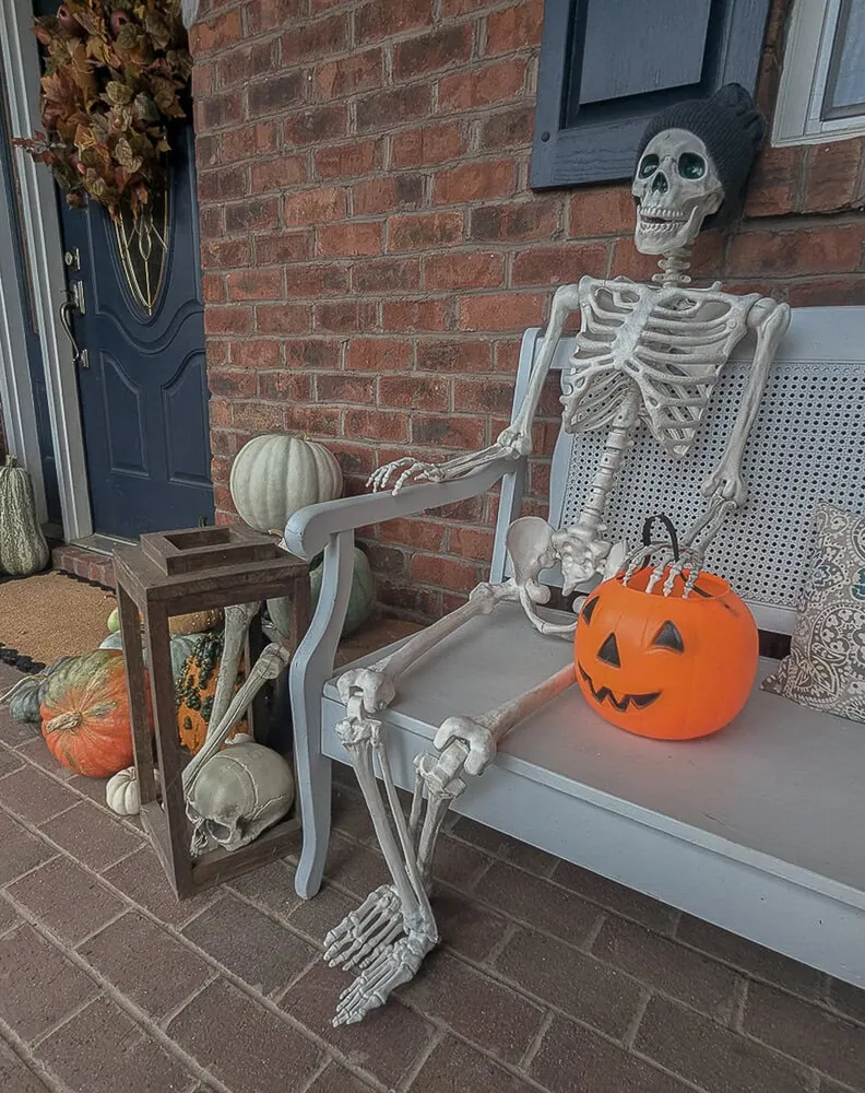 fake skeleton sitting on bench on front porch.